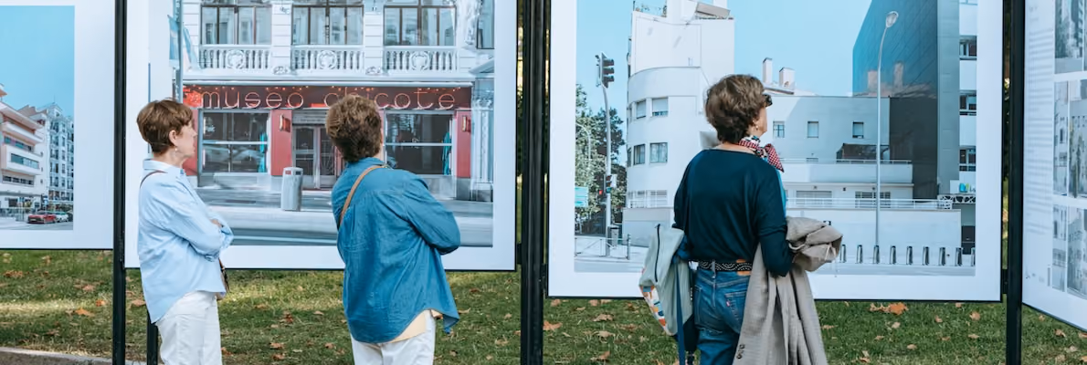 Three women viewing photographs depicting buildings outdoors during Madrid Architecture Week