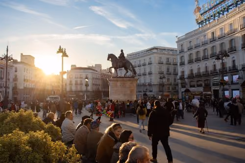 Puerta del Sol in Madrid at sunset, with the equestrian statue and crowds in the square.