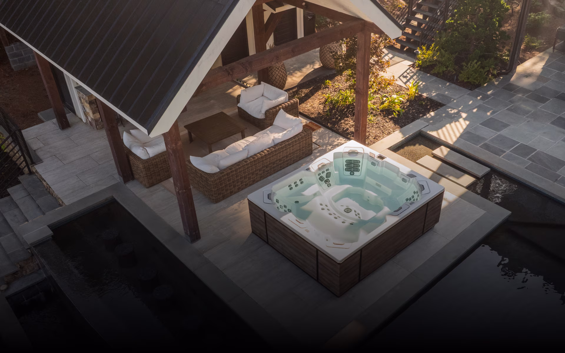 Outdoor patio area with a modern hot tub next to wicker furniture under a shaded pergola.