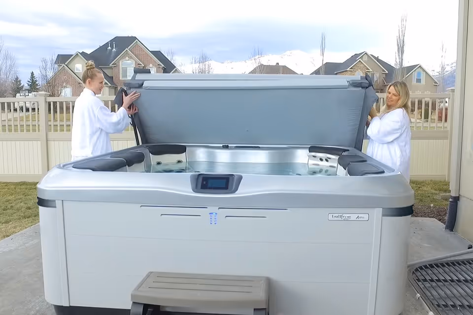 Two women removing a cover from a spa tub.