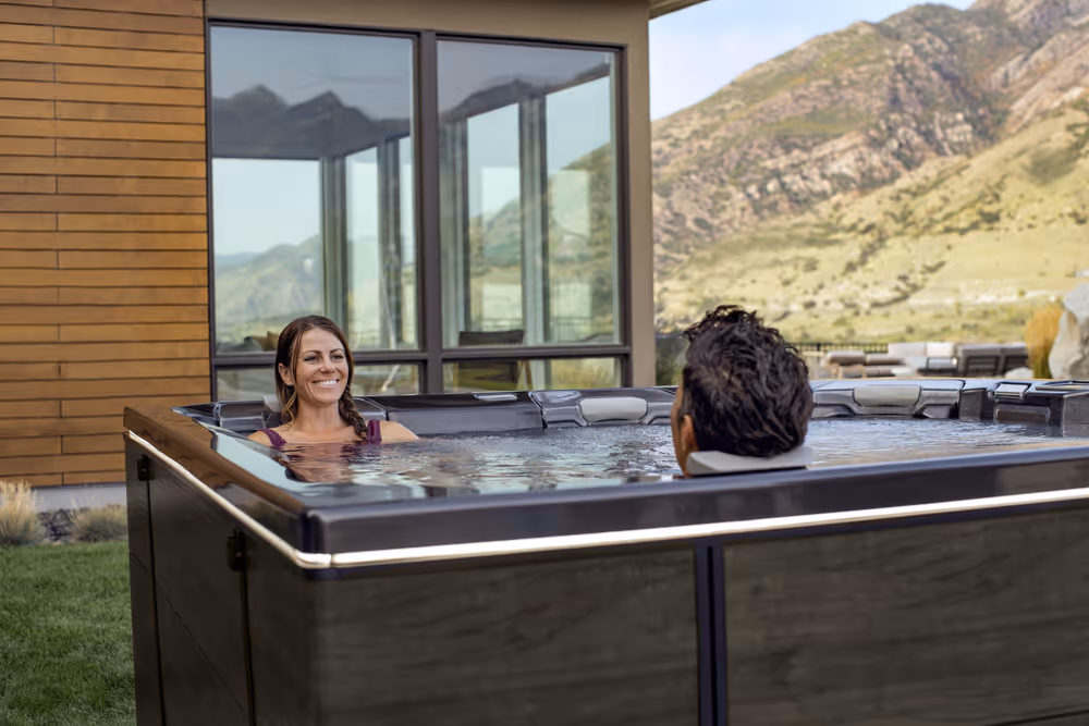 A couple sitting in an M series spa tub with a mountain backdrop.