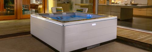 A STIL series spa in a patio behind an upscale home with full height windows.