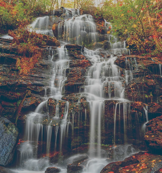 Multi-tiered waterfall cascading over rocks surrounded by autumn foliage.