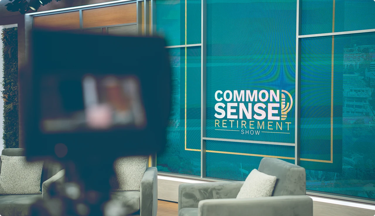 TV studio set with a large screen displaying the words 'Common Sense Retirement Show' and two gray armchairs with pillows.