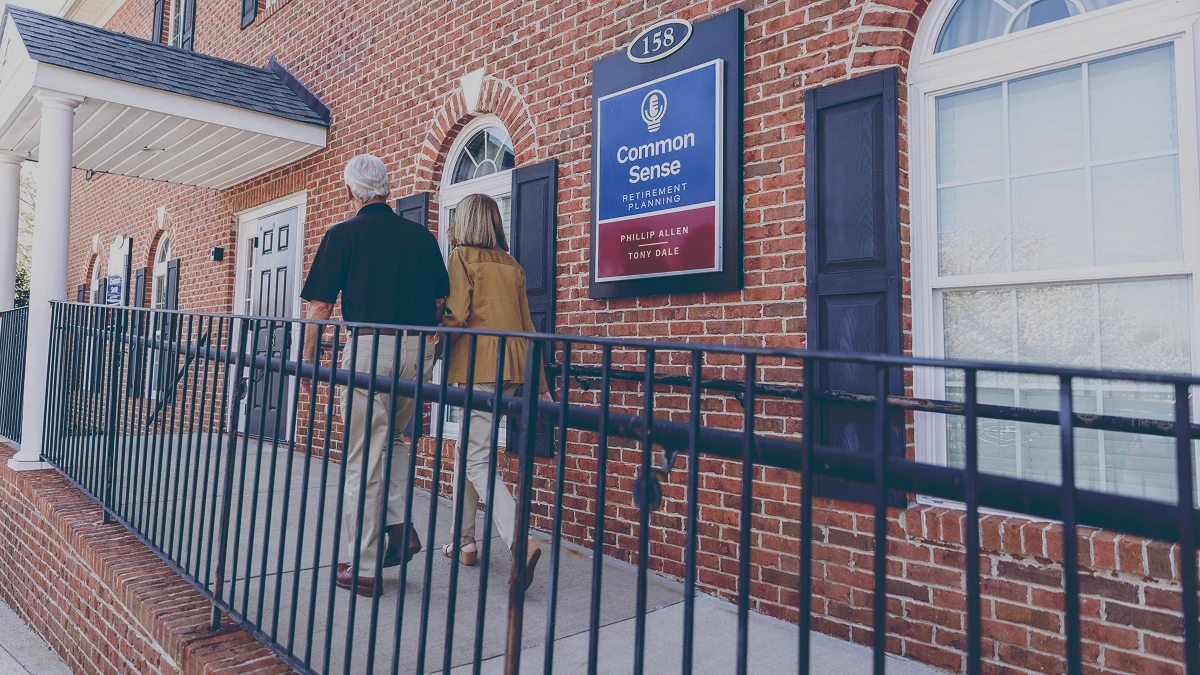 Retired couple walking up a ramp to a brick building with a sign that reads Common Sense Retirement Planning.