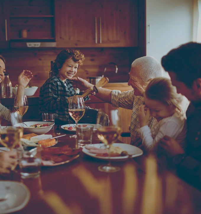 Smiling multigenerational family enjoying a meal together in a warm kitchen setting.