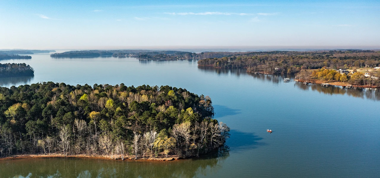 Aerial view of a calm lake surrounded by forested land with a small boat on the water.