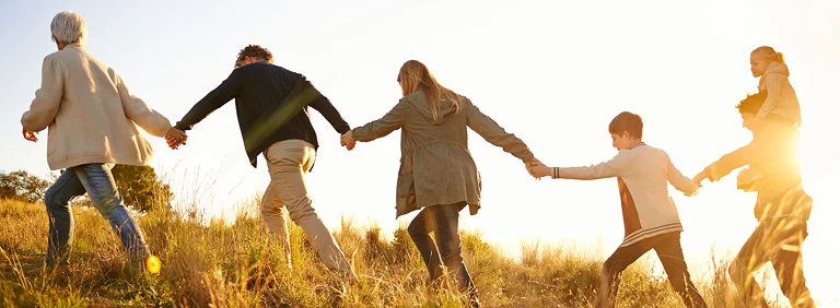 multigenerational family walking up a grass covered hill at dusk