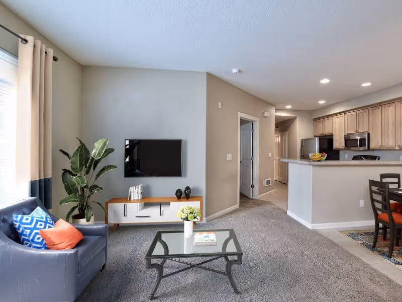Virtually staged living area with sofa, coffee table, tv, and large window featuring view of kitchen