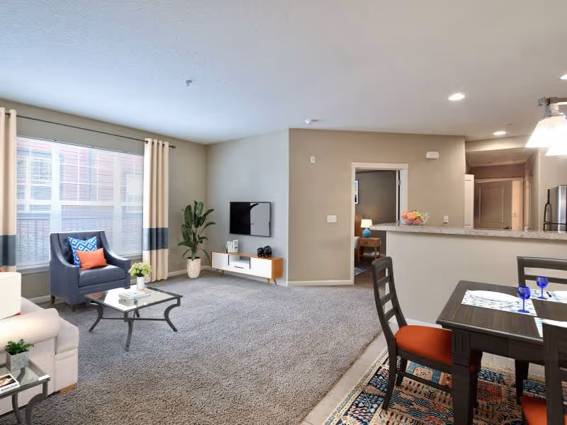 Virtually staged living area with sofa, coffee table, tv, and large window featuring view of dining area with table chairs