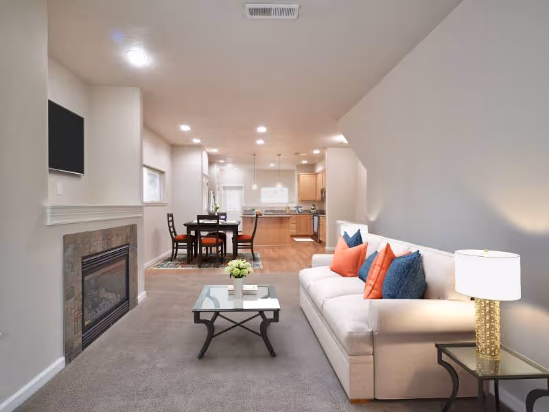 Virtually staged living area with sofa, coffee table, tv, fireplace and large window featuring view of kitchen