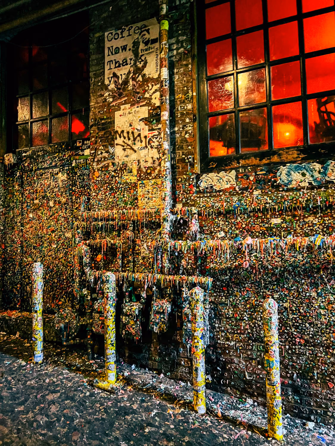 Brick wall and poles covered in chewed gum with two red-lit windows above at night.