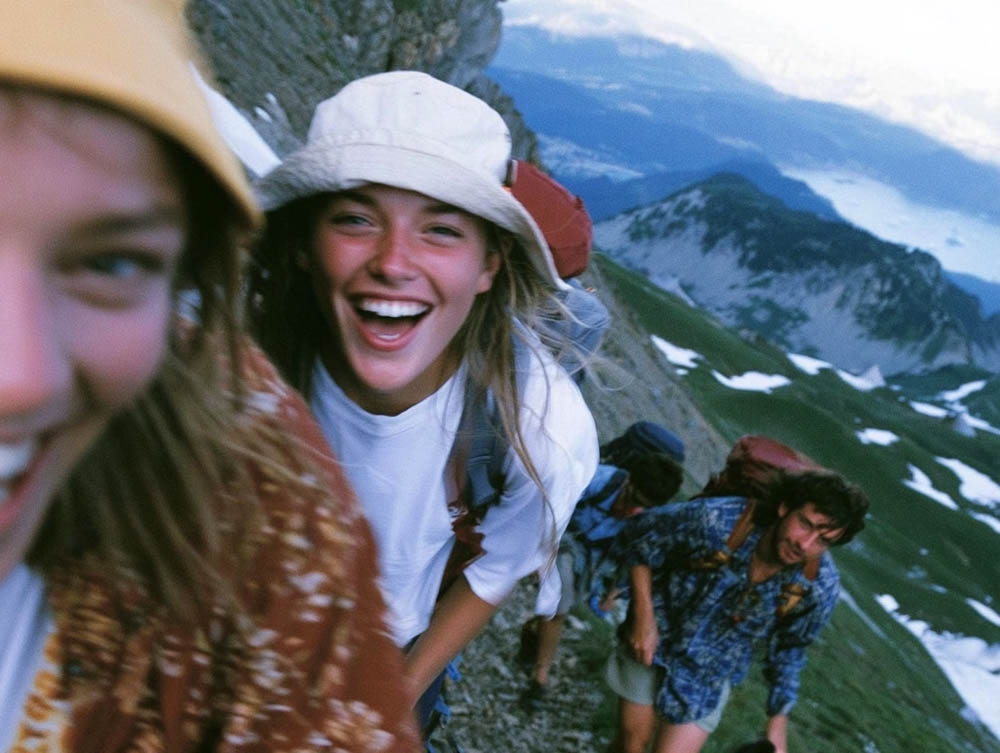 Group of hikers climbing a mountain trail with snowy peaks and valleys in the background.
