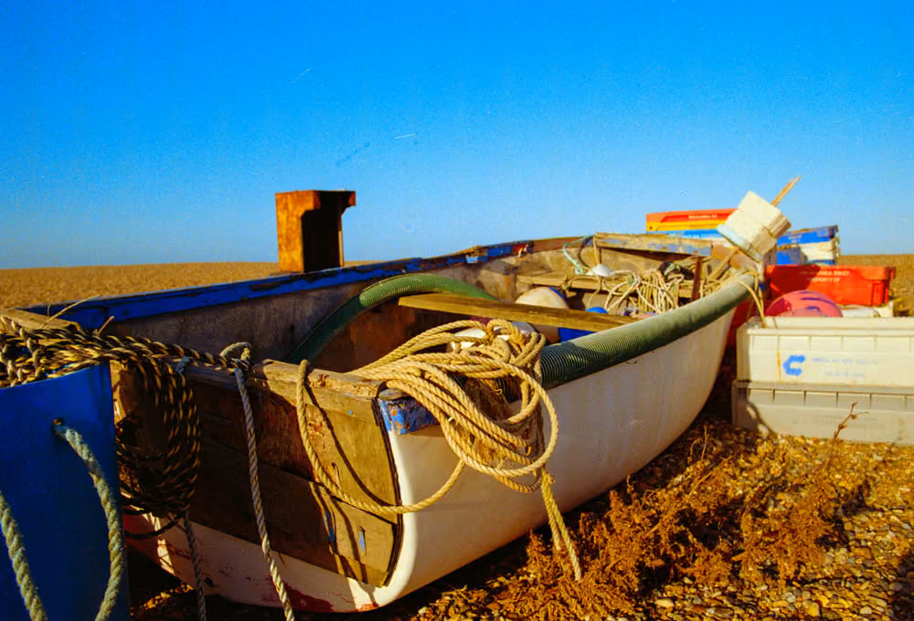 Fishing boat on pebble beach with ropes, crates, and clear blue sky at sunset.