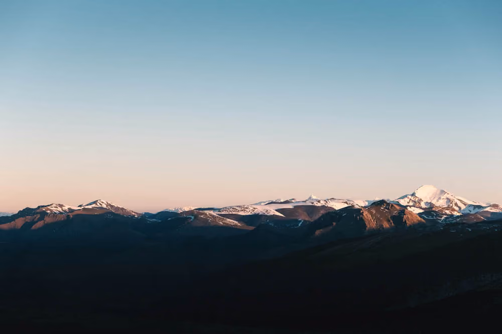 Distant snow-capped mountains under a clear sky during sunrise or sunset.