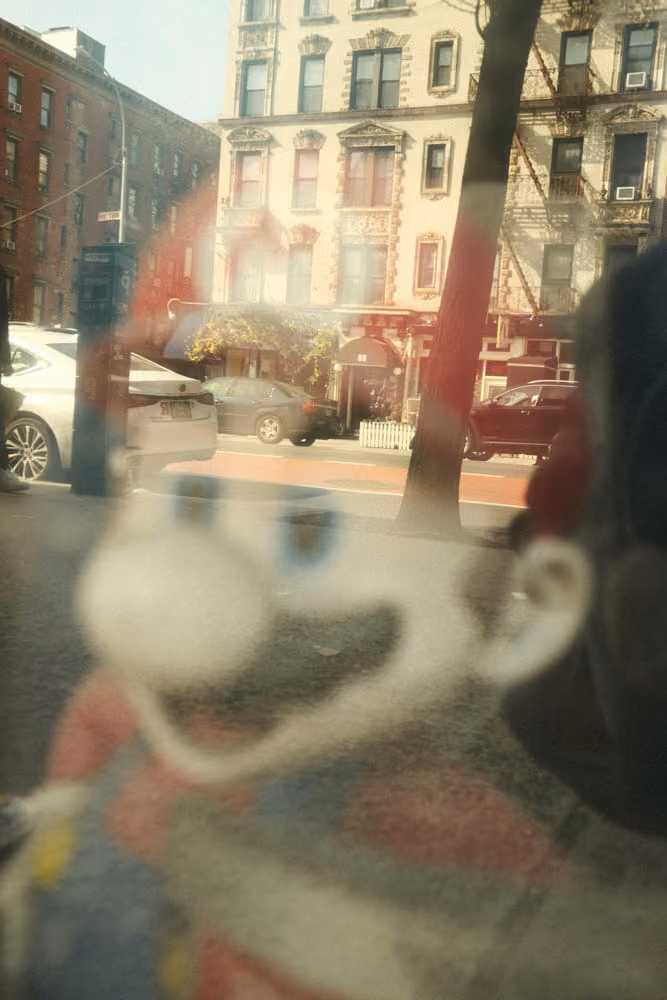 Blurred reflection of a cartoon character on a city street with cars and buildings in sunlight.