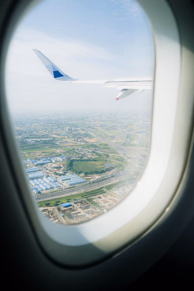 View of an airplane wing and a city landscape below from an airplane window in flight.