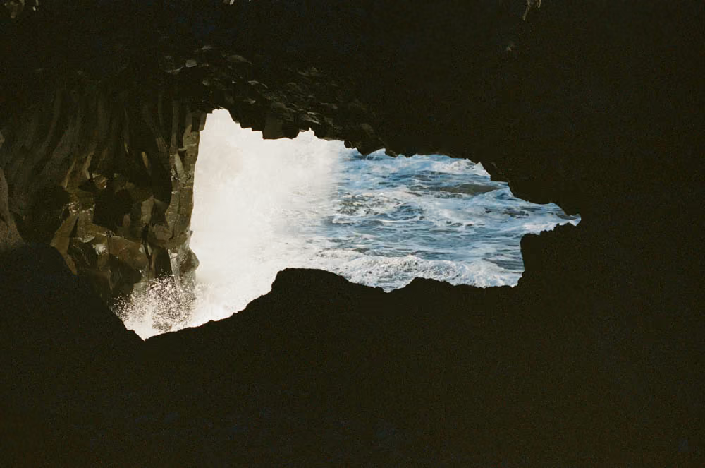 Ocean waves crashing against jagged rocks, viewed through a dark cave opening.