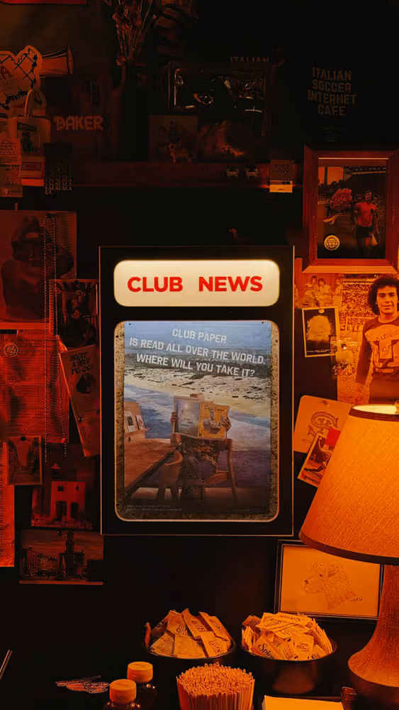 A dimly lit wall with a 'CLUB NEWS' display and vintage photos surrounding a lamp and condiment bottles.