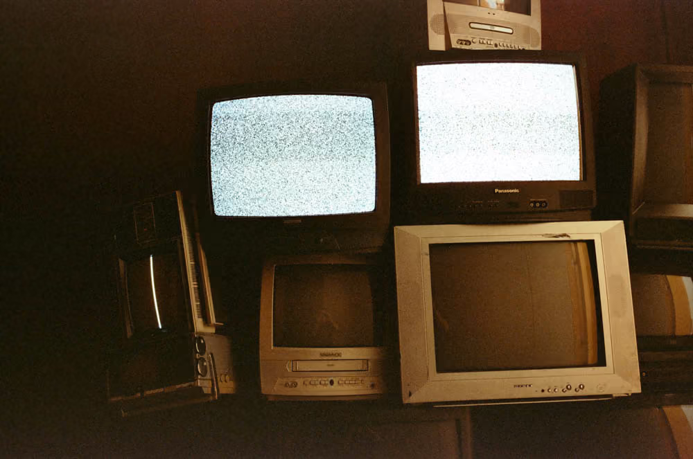 Stack of old CRT televisions, two showing static screens, others turned off in dim light.