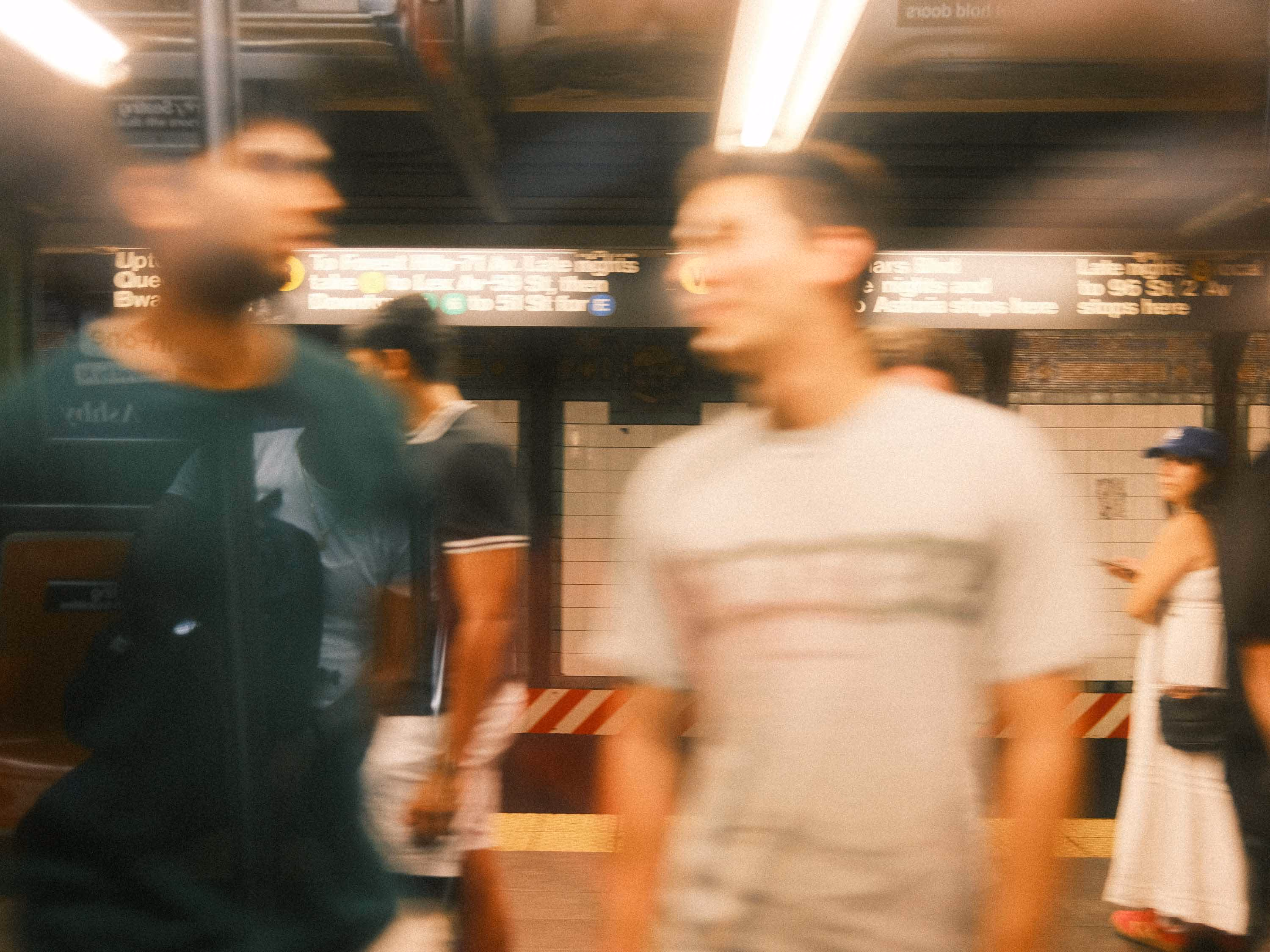 Blurred people walking in a subway station with a woman standing by the wall in the background.