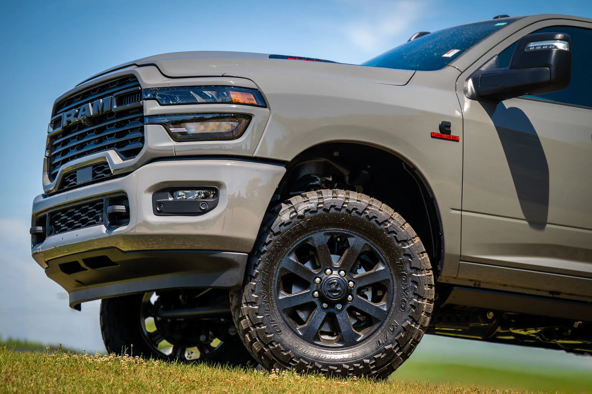 front quarter view of a silver ram 2500 cummins turbo diesel with black wheels and toyo open country mud-terrain tires on a grassy hill