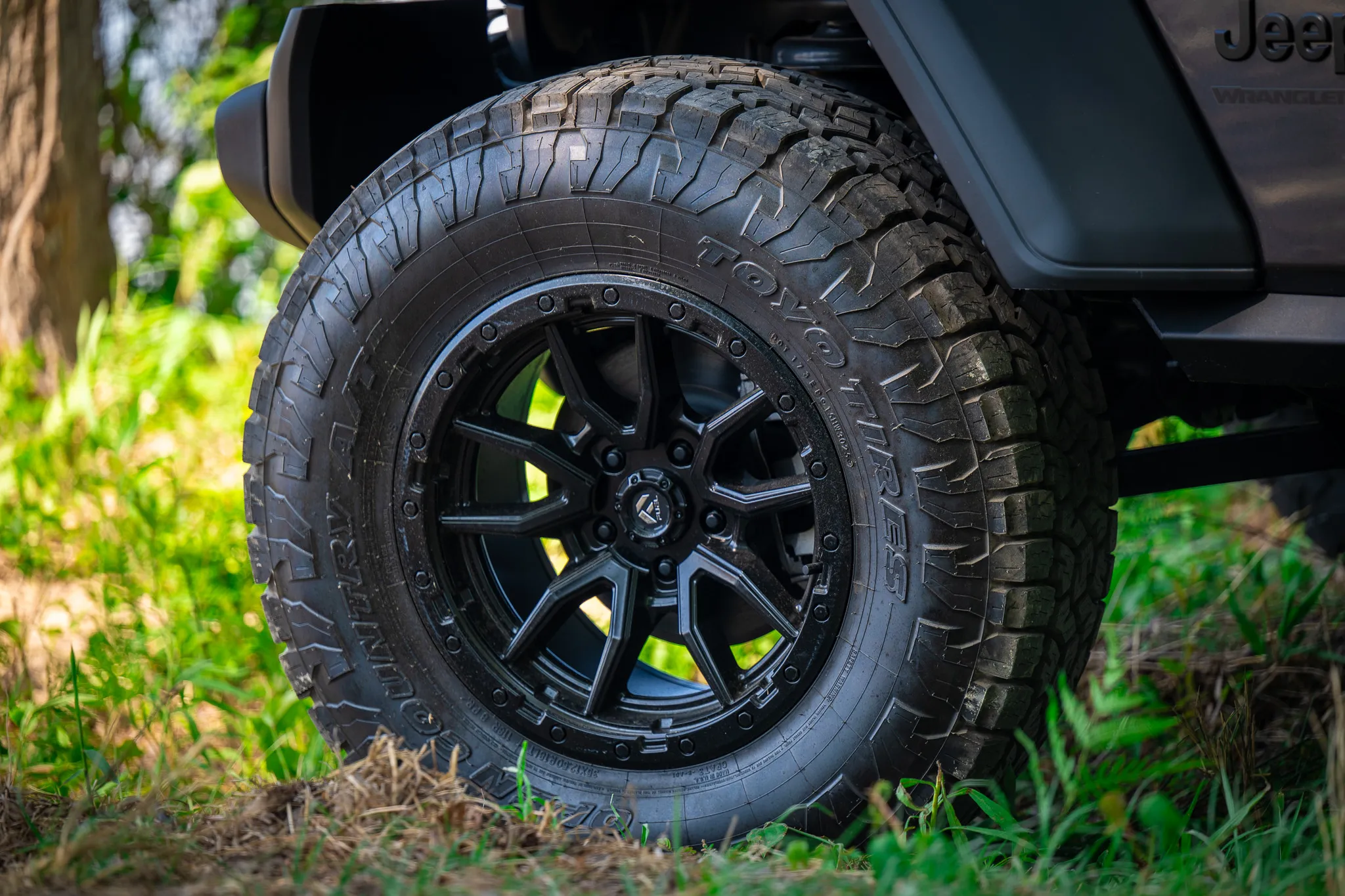 Close-up of a black fuel off-road wheel with toyo open country all-terrain tire mounted on a dark gray jeep wrangler, parked on grass