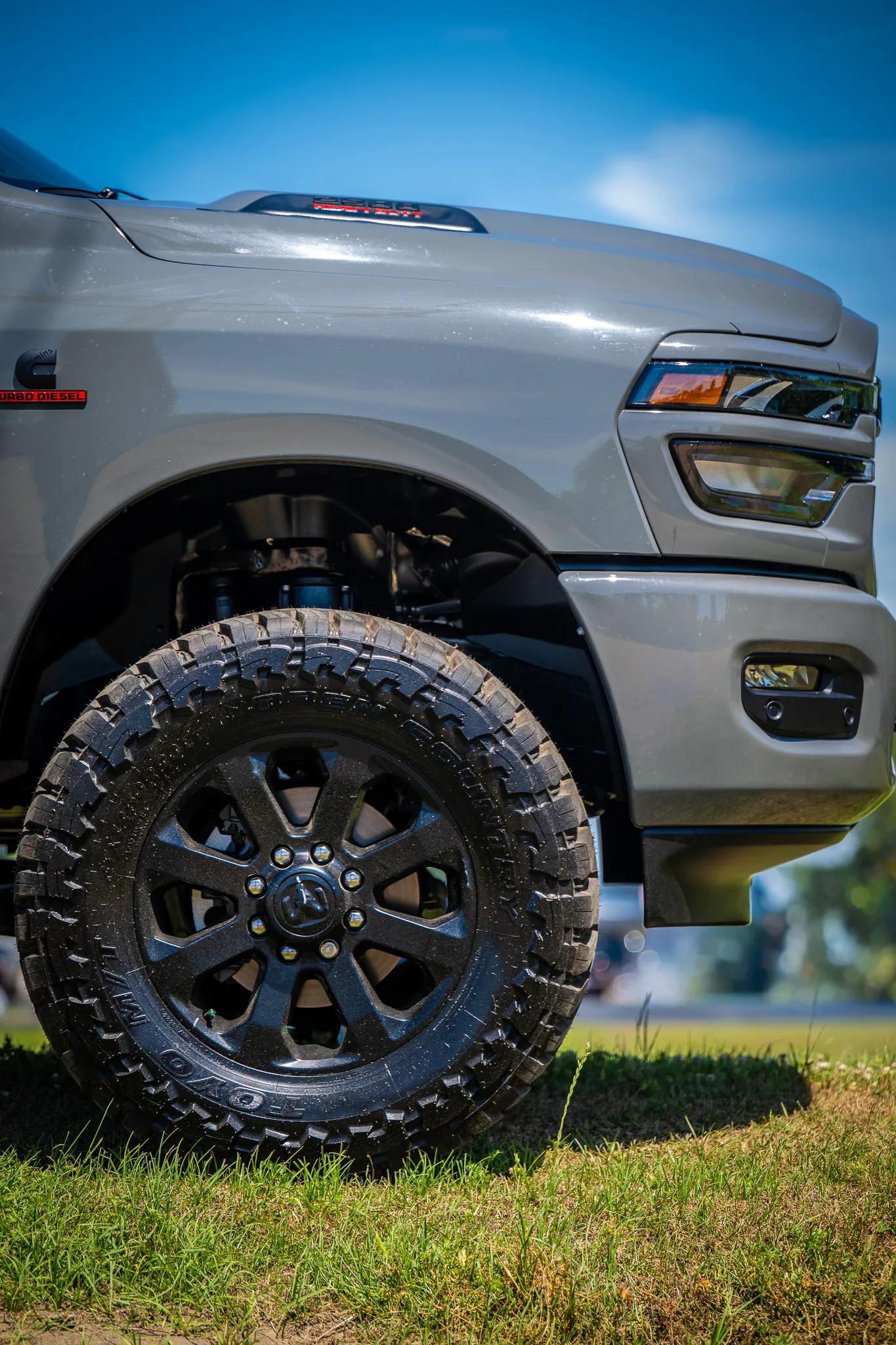 Close-up of a silver Ram truck front wheel well showing a black off-road wheel with Toyo mud-terrain tires and a Cummins Turbo Diesel badge on the fender