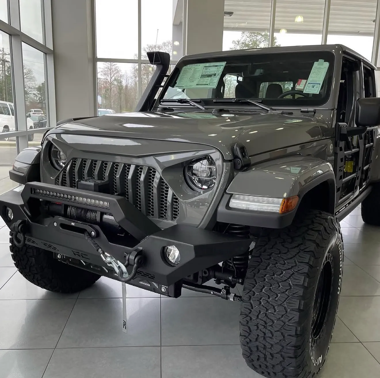 gray jeep wrangler unlimited in a dealership showroom with a rough country front bumper, led light bar, winch, snorkel, and bfgoodrich all-terrain tires