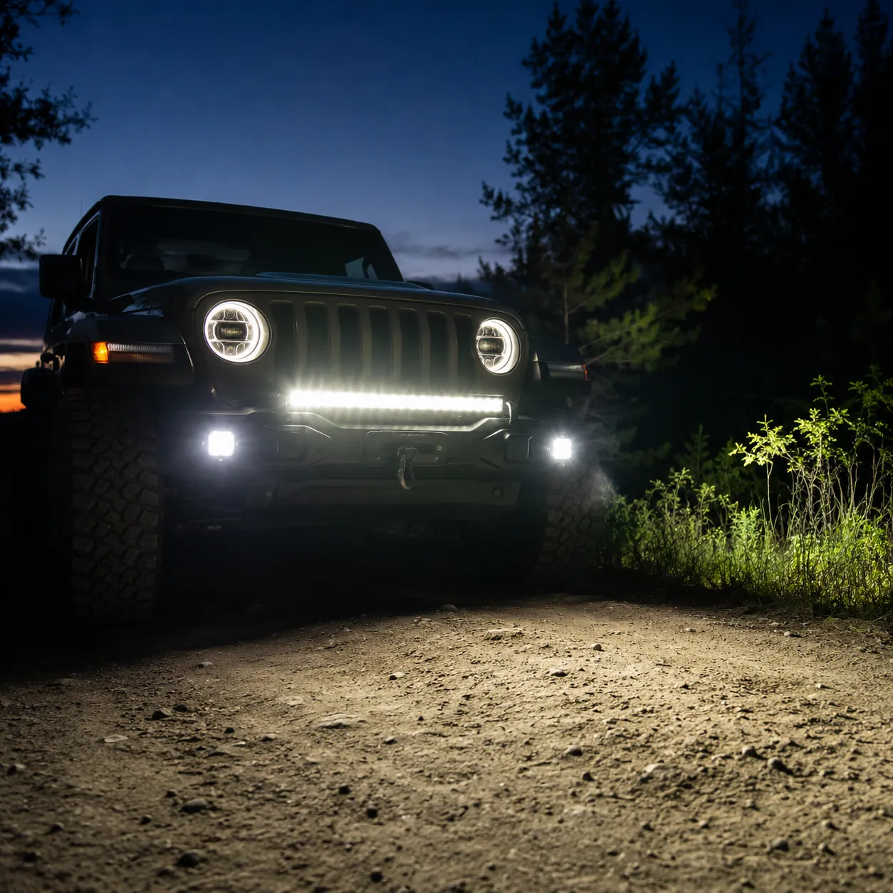 jeep wrangler on a dirt trail at dusk with an led light bar, auxiliary pod lights, and halo headlights illuminating the path ahead