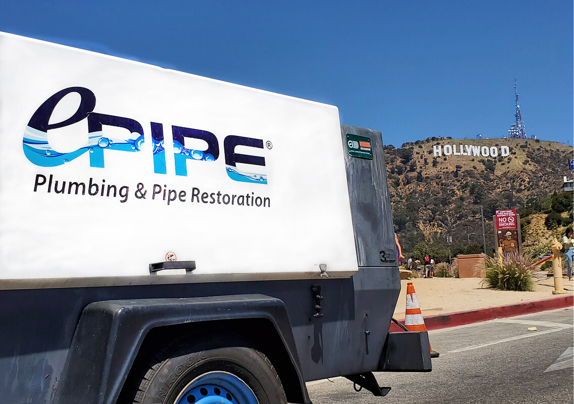 White and gray trailer with ePIPE Plumbing & Pipe Restoration logo parked near the Hollywood sign on a sunny day.