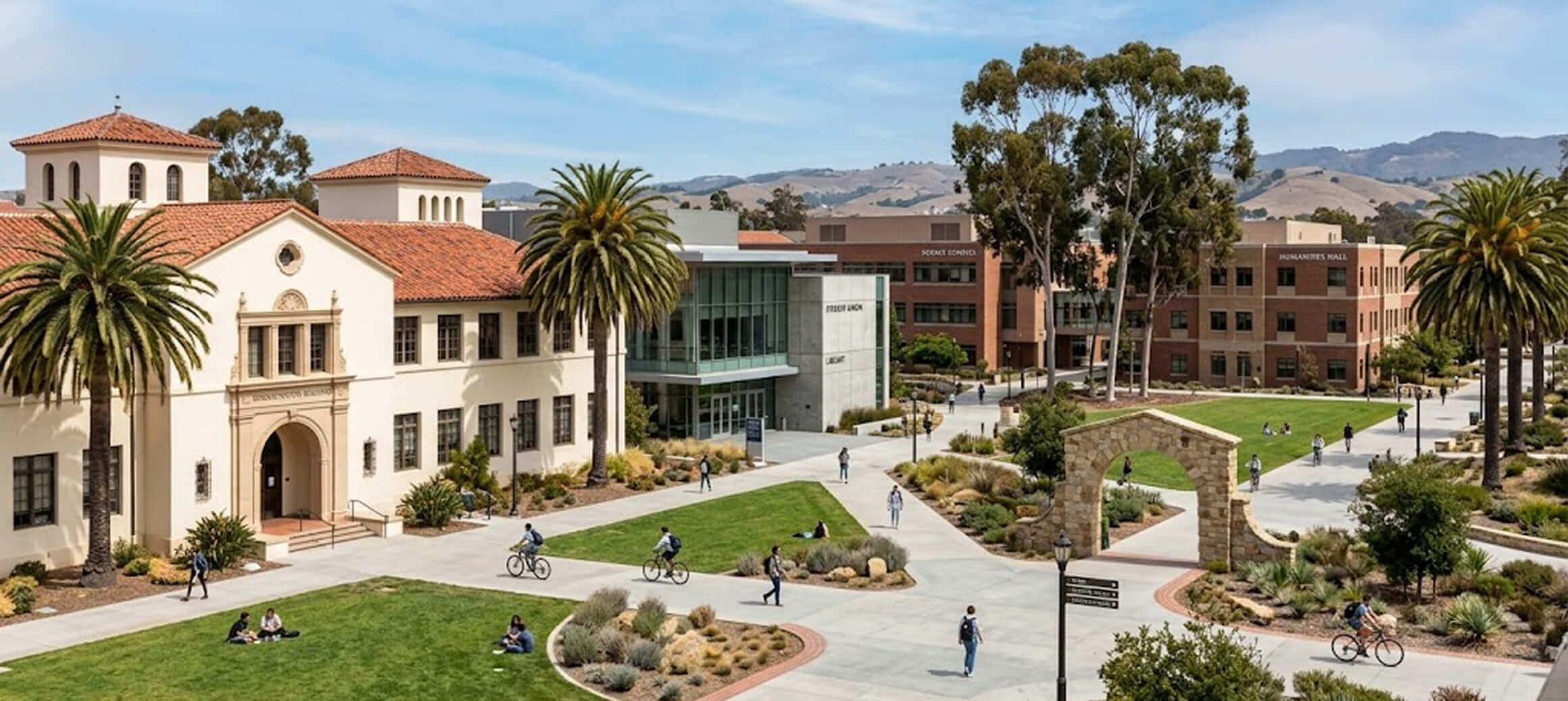 University campus with students walking and biking on pathways amidst historic and modern buildings under a blue sky.