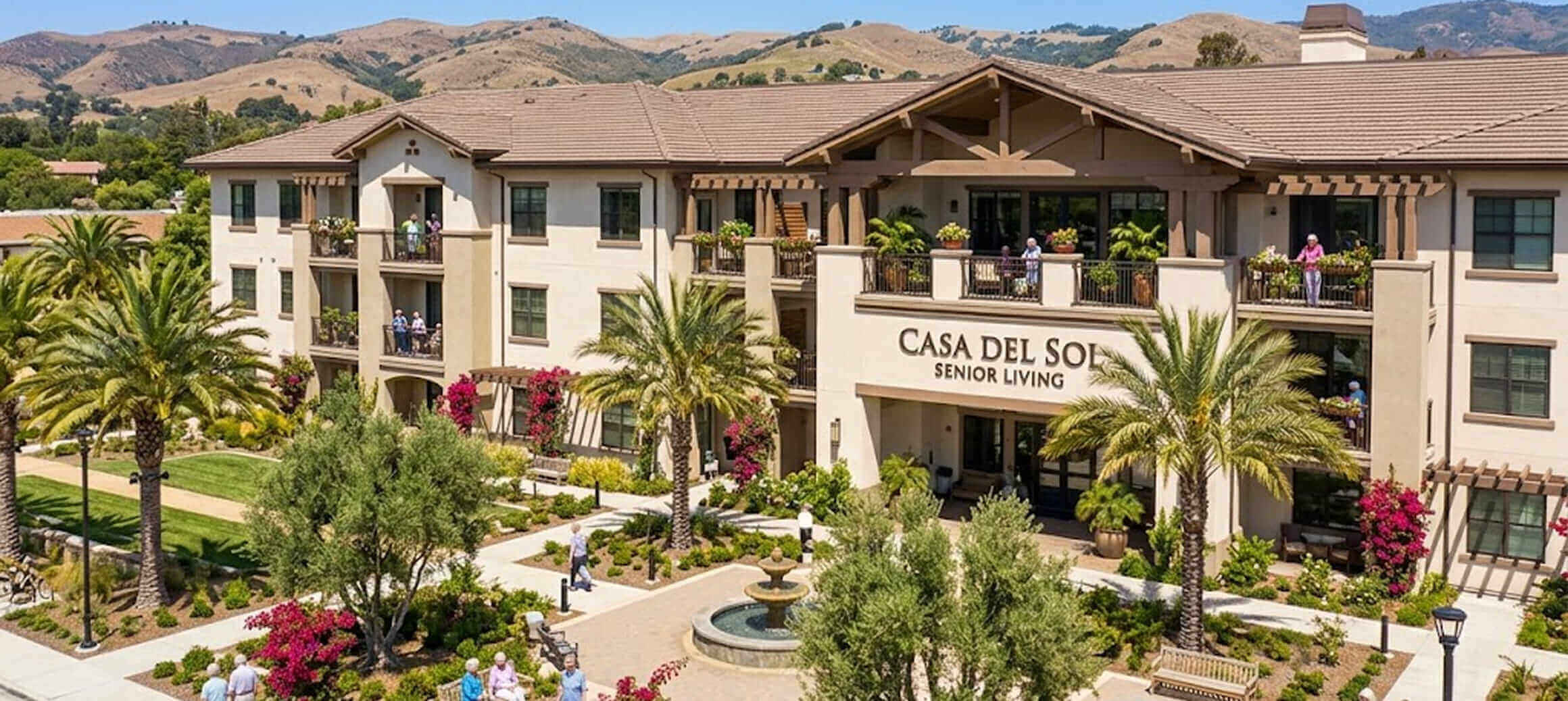 Casa Del Sol Senior Living building with palm trees, garden, fountain, and people on balconies and walking outside.