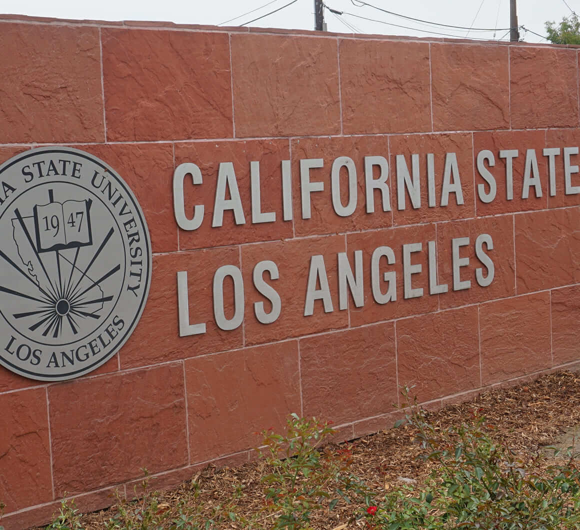 Sign on a red brick wall reading California State University Los Angeles with the university seal showing an open book and the year 1947.