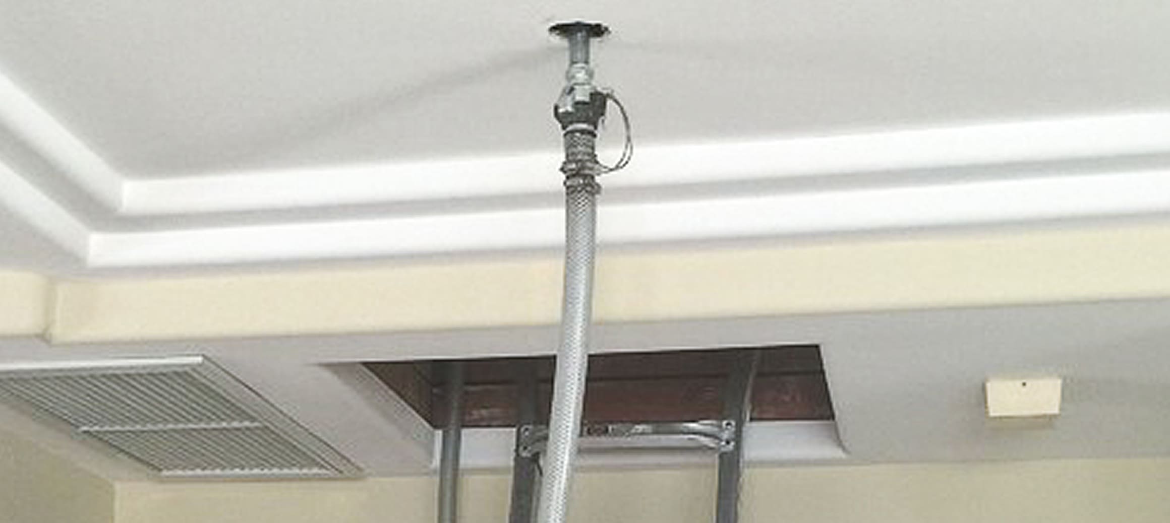 Ceiling-mounted fire sprinkler pipe with a flexible metal hose connected to an open ceiling panel.