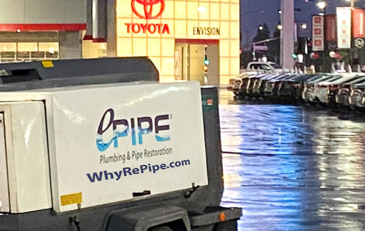 Vehicle trailer with Opipe Plumbing & Pipe Restoration and WhyRePipe.com signage in front of a Toyota dealership at night.