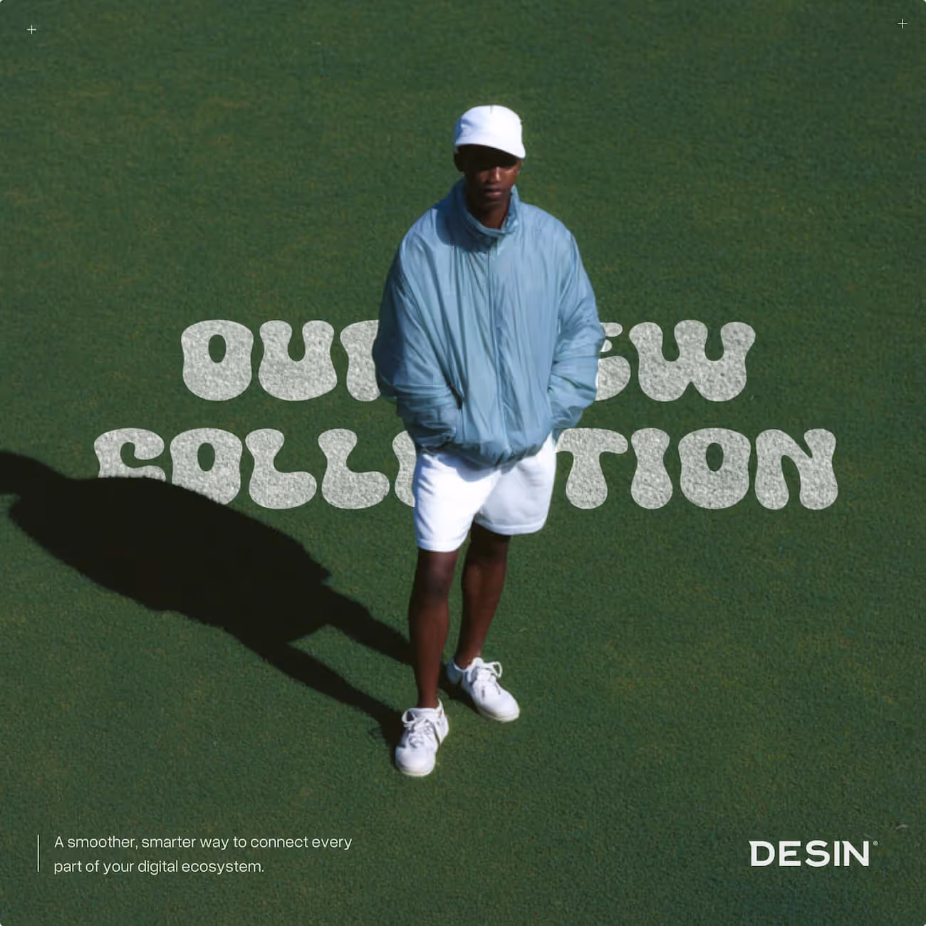 Man wearing a light blue jacket, white shorts, and white cap standing on green grass with 'OUR NEW COLLECTION' text behind him.