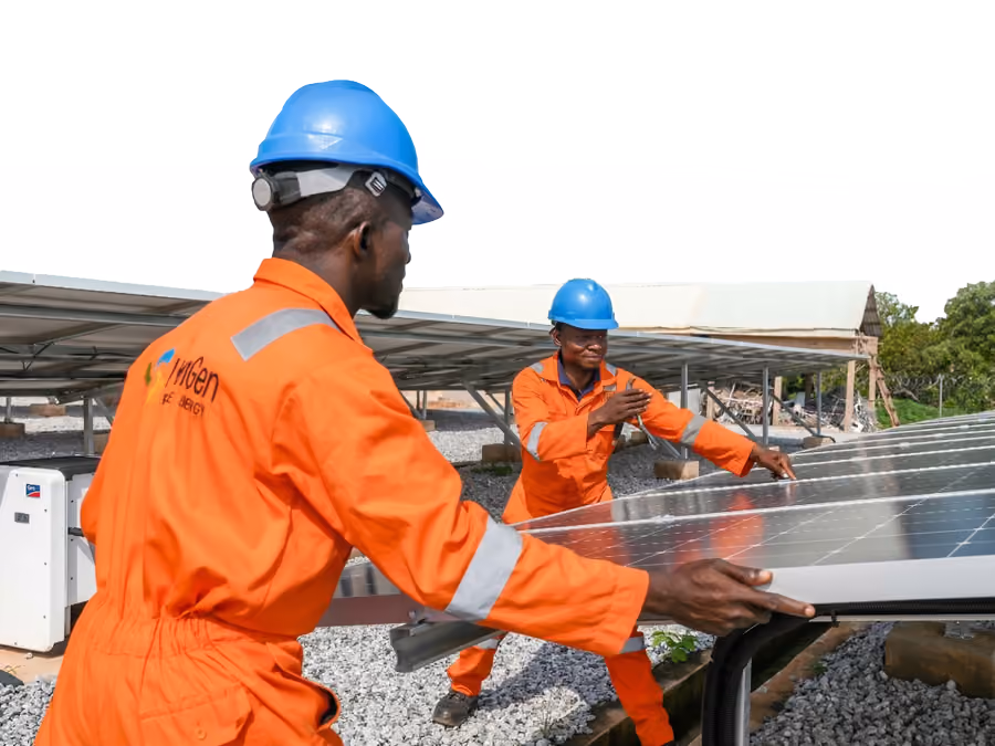 Two engineers in orange overalls and hard hats fit a solar panel at a mini grid site in Nigeria