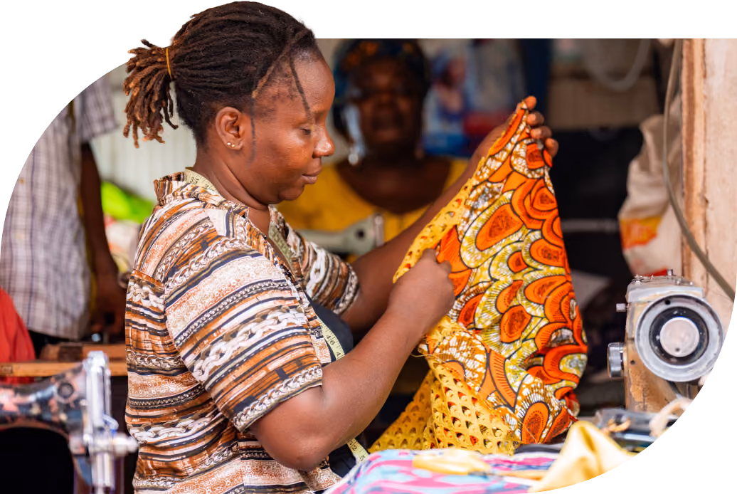 Seamstress Mary Alaele Baelanki holds up patterned fabric at her stall in Wuse Market, Abuja, which received mini grid electricity in 2024
