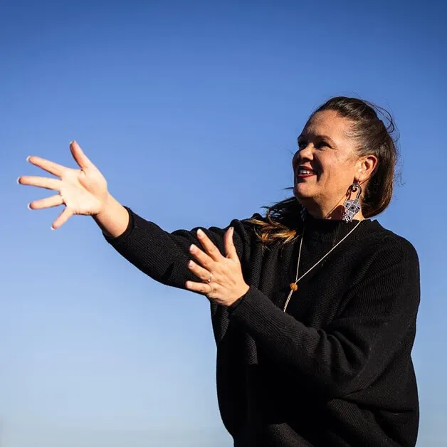 Indigital team member speaking outdoors, hand outstretched, blue sky behind