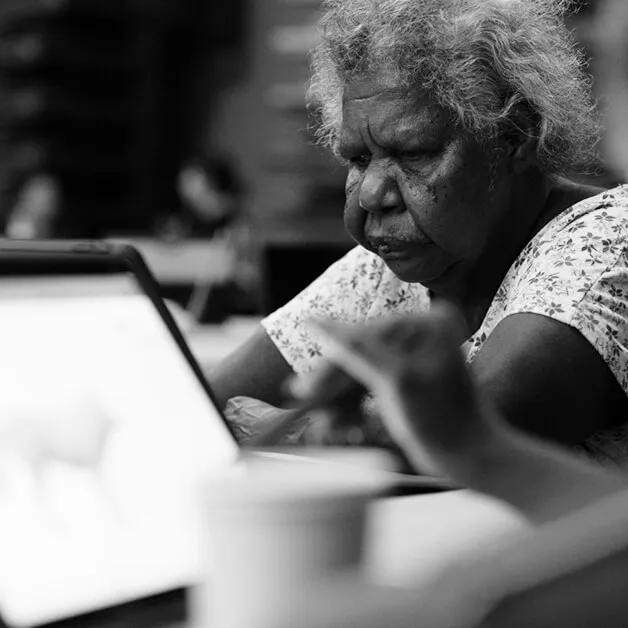 First Nations Elder reviewing work on a laptop, black-and-white photograph