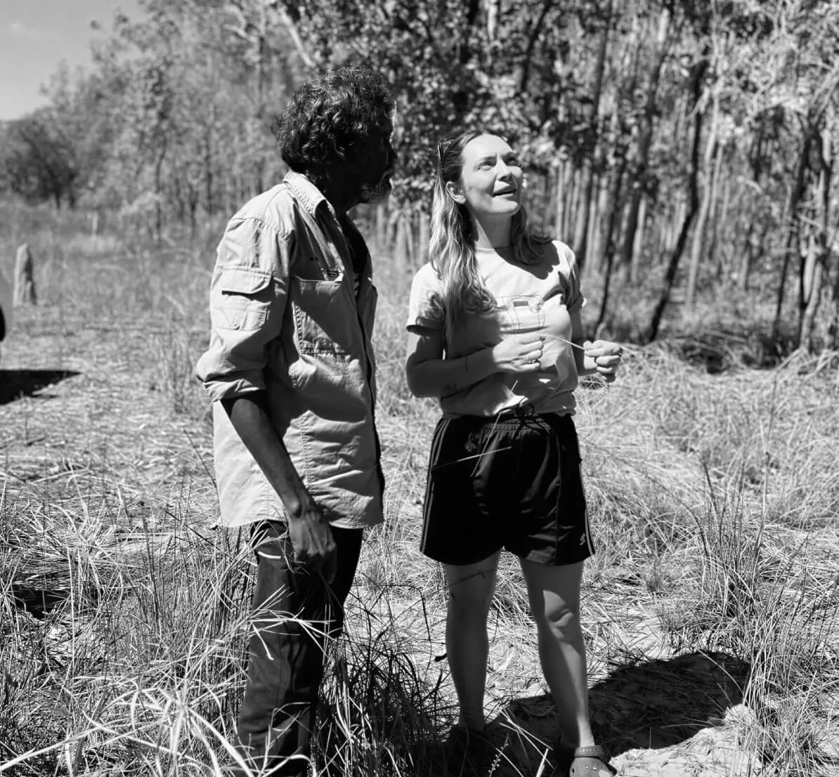 Two people in conversation on Country, dry grassland behind them, black-and-white photograph