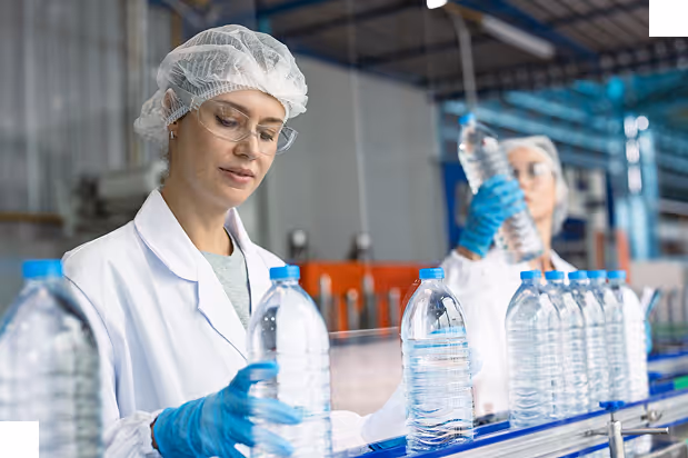 Factory workers in protective gear inspecting plastic water bottles on a production line.