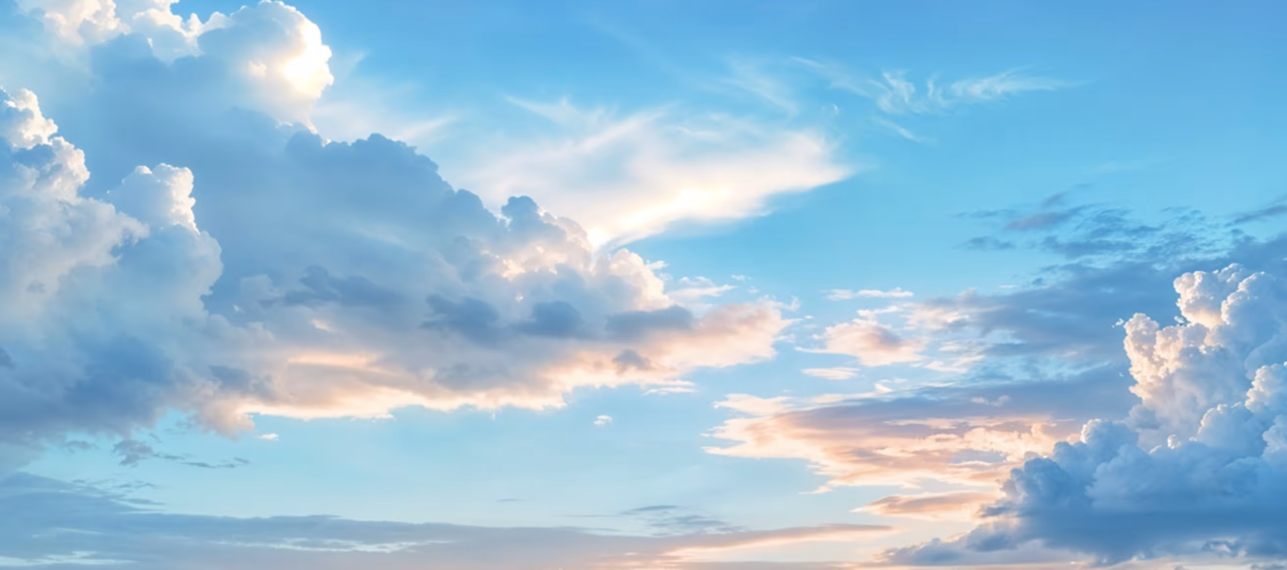 Blue sky with large fluffy clouds illuminated by soft sunlight at sunset.