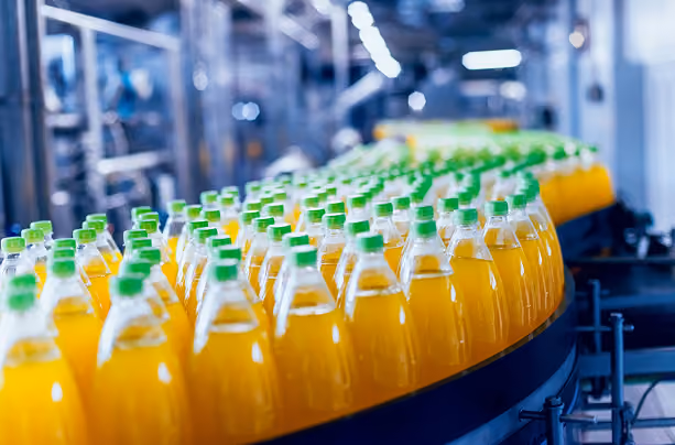 Rows of orange soft drink bottles with green caps on a factory conveyor belt.