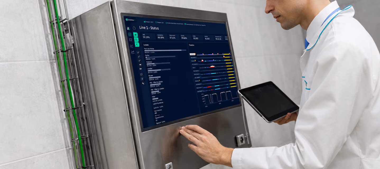 Man in lab coat using touchscreen panel and holding tablet showing industrial line status data.