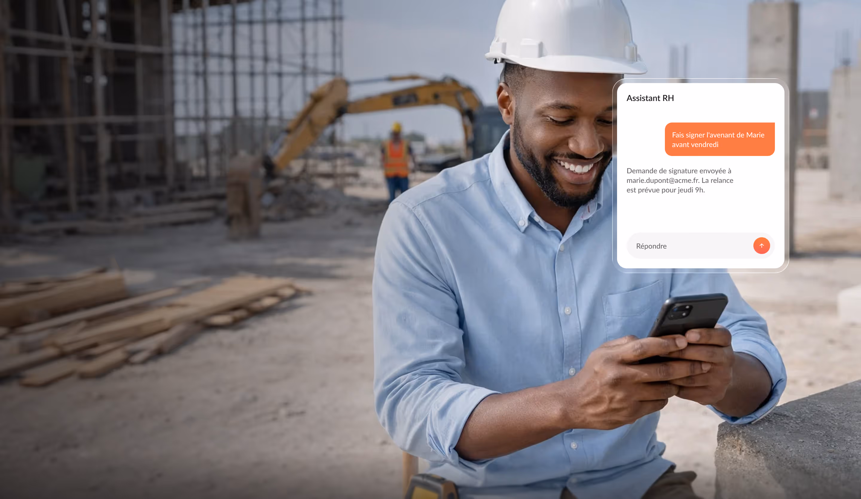 Smiling construction worker wearing a white helmet and blue shirt using a smartphone on a building site with construction machinery in the background.