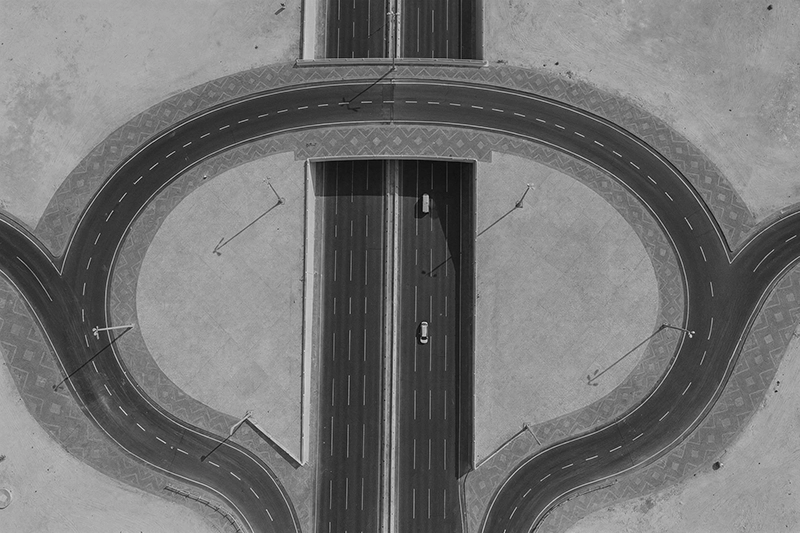 Aerial view of a highway interchange with a cloverleaf loop and two cars on a multi-lane road. Dukhan Highway, Qatar.