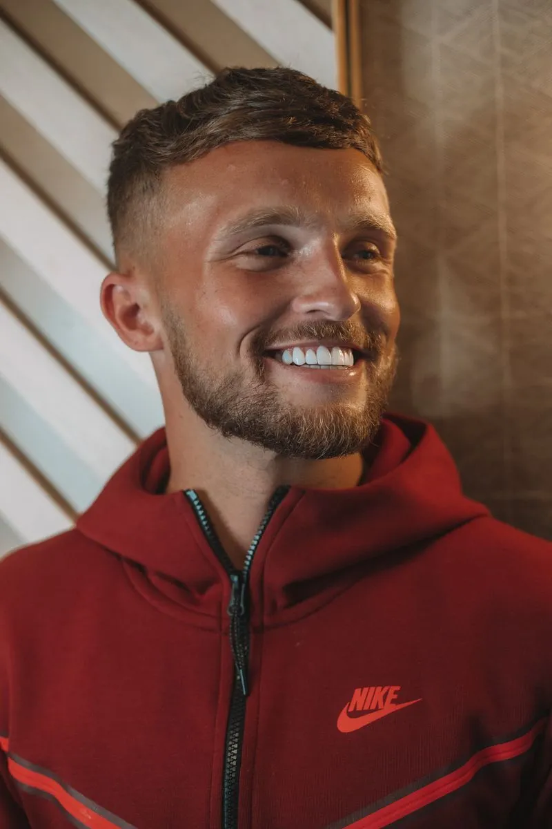 A man with a beard wearing a red nike hoodie, smiling.