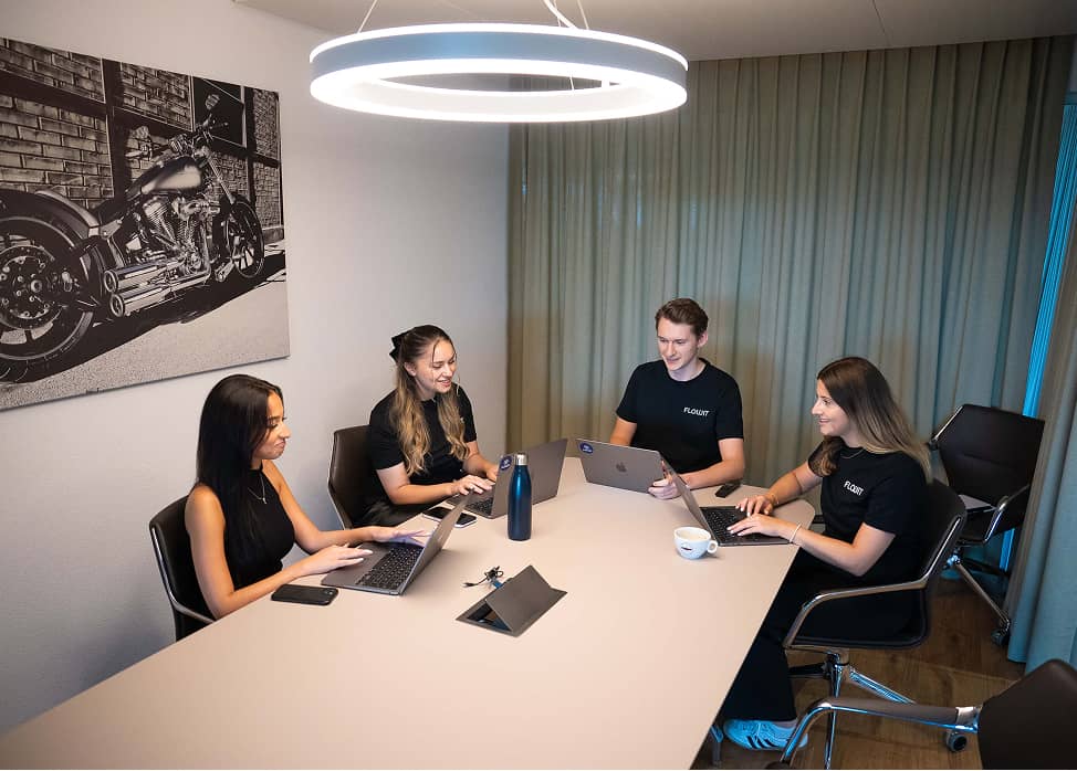 Four people wearing black shirts working on laptops around a conference table under a round light.
